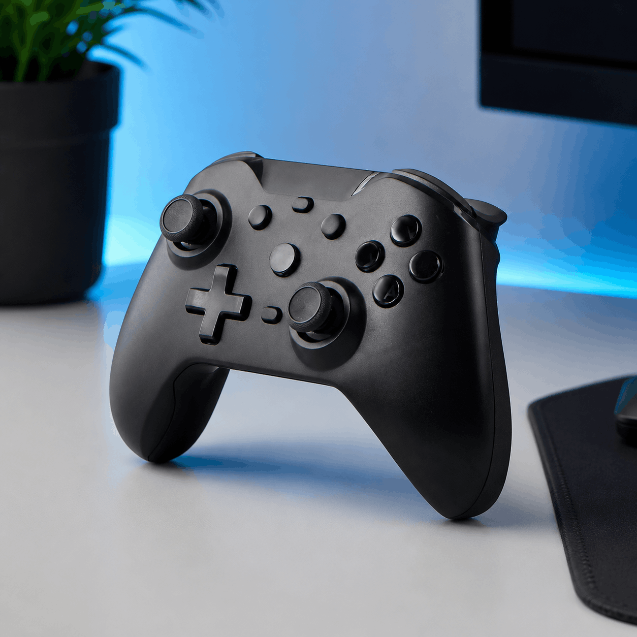 Black ergonomic Bluetooth game controller in a clean modern desk setup with blue accent lighting